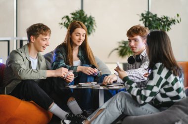 Dört üniversite öğrencisi boş zamanlarının tadını çıkarırken rahat koltuklarda dinleniyorlar.