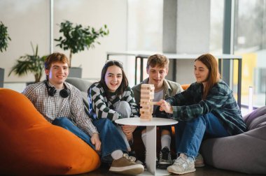 Dört genç öğrenci puf minderlerinde oturmuş, blok oyunu oynarken eğleniyorlar.