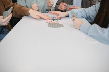 Mutlu arkadaşlar beyaz bir masanın etrafında toplanmış, neşe dolu bir kart oyununun tadını çıkarıyorlar.