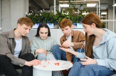 Dört genç yetişkin bir masada oturmuş masa başında oyun oynuyor ve birlikte vakit geçiriyorlar.