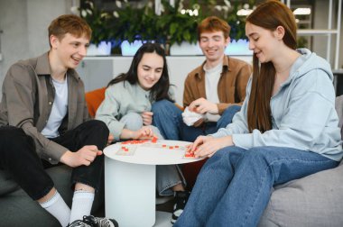 Bir grup genç arkadaş bir masa oyunu oynuyor, kahkahaları paylaşıyor ve içeride harika vakit geçiriyorlar, arkadaşlığı ve boş zamanları ön plana çıkarıyorlar.