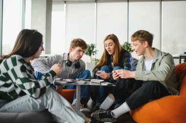 Dört üniversite öğrencisi küçük bir masanın etrafında oturuyor, iskambil oynuyorlar ve üniversitenin dinlenme odasında birlikte eğleniyorlar.