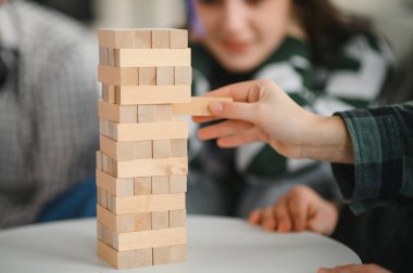 Heyecan ve gerilim dolu arkadaşlarla eğlenceli bir oyun oynarken, bir kadın dikkatli bir şekilde tahta bloğu riskli bir kuleden kaldırıyor.
