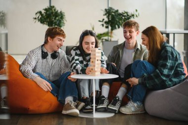 Dört genç meslektaşı mola veriyor, blok istifleme oyunu oynuyorlar ve rahat koltuklarla modern ofis alanında birlikte eğleniyorlar.