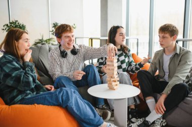 Bir grup neşeli genç yetişkin evlerinde odun blokları istifleme oyunu oynayarak eğleniyor.