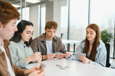 Modern bir ofiste mola verirken kağıt oynayan dört meslektaş, dostluğu ve rahatlığı teşvik ediyor.