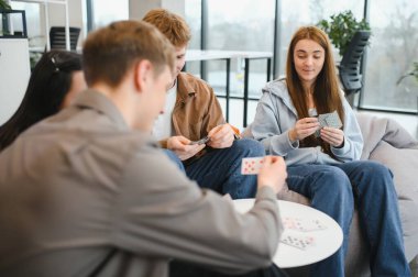 Bir grup genç meslektaşın ofis molasında kart oynuyorlar, arkadaşlığı ve rahatlığı teşvik ediyorlar.