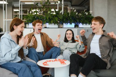 Oyun oynayan dört neşeli arkadaş, zaferlerini modern ofis alanında kutlarken heyecan ve mutluluk ifade ediyorlar.