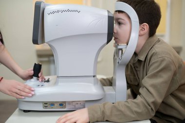 Oftalmolog, modern bir göz kliniğinde genç bir çocuğun vizyonunu kontrol etmek için otomatik fraktör kullanıyor.