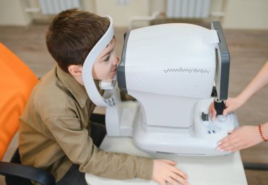Modern bir klinikte otoptalmolog bir çocuğun görme duyusunu otoportraktör kullanarak inceleyerek görme kontrolü ve bakımı üzerinde çalışıyor.