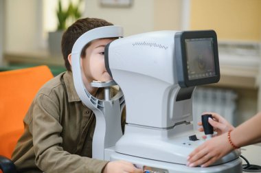 Oftalmolog, bir klinikte bir çocuğun görme yeteneğini otomatik fraktörle inceleyerek, düzgün bir görme ve sağlık kontrolü sağlar.