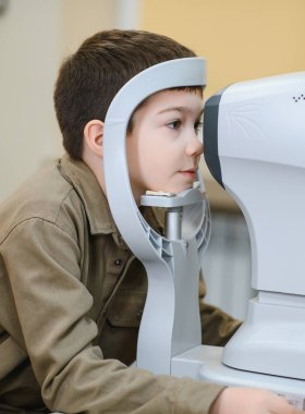 Göz hekimliği kliniğinde görme testi sırasında otomatik fraktör kullanan çocuk, görme keskinliğini ve kırılma hatalarını kontrol ediyor