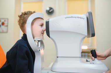 Oftalmolog, klinikteki genç bir çocuk üzerinde görüş kontrolü yapmak için modern bir oto-fraktör kullanıyor.