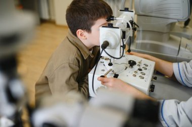 Modern bir oftalmoloji kliniğinde bir çocuğun görme yeteneğini inceleyen oftalmolojist, kesin görme ve bakım tanılarını güvence altına alır.
