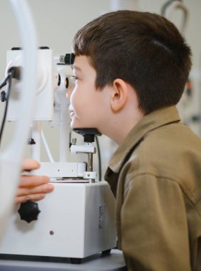 Bir tıp kliniğinde modern bir oto-fraktör kullanan genç bir çocuğun görme duyusunu inceleyen oftalmolog.