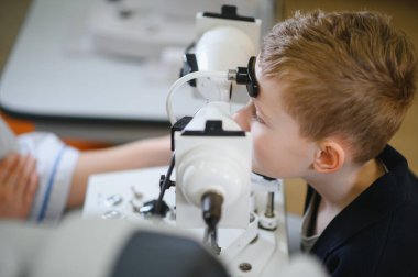 Görme engelli çocuk görme kliniğinde phoropter kullanan bir göz doktoru tarafından kontrol ediliyor.