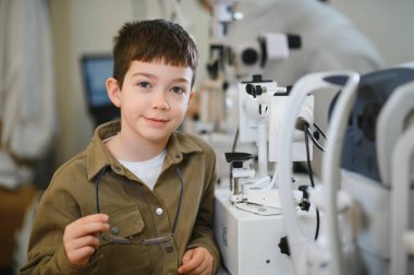Genç bir çocuk modern bir göz kliniğinde göz muayenesi sırasında gözlük takıyor.