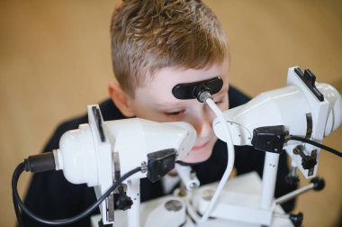 Bir göz doktoru tarafından görme kontrolüne tabi tutulan genç bir çocuk, ileri düzey tıbbi ekipmanlar kullanarak doğru teşhis ve görme bakımı yapıyor.
