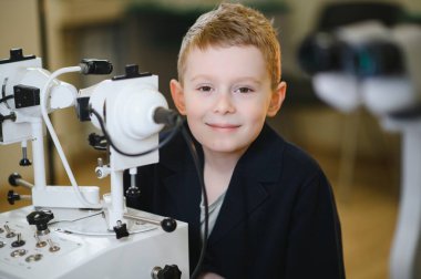 Modern bir göz hastalıkları kliniğinde ileri seviye teşhis cihazları kullanarak çocuk göz sağlığını vurgulayan bir vizyon kontrolü sırasında gülümseyen genç çocuk