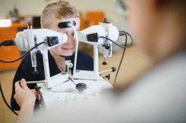 Modern bir klinikte bir göz doktoru tarafından yürütülen ileri seviye teşhis cihazlarıyla vizyon kontrolünden geçen genç bir çocuk.