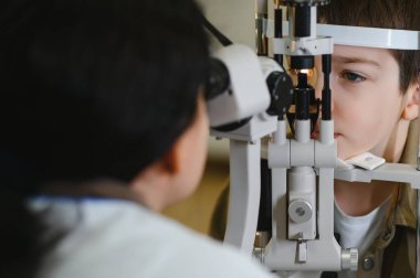 Çocuk modern bir klinikte profesyonel bir göz doktoru tarafından kesik lamba biyomikroskobu kullanılarak göz muayenesinden geçiriliyor.