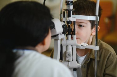 Bir klinikte phoropter kullanan bir çocuğun görüşünü kontrol eden oftalmolog, doğru teşhis ve göz sağlığı değerlendirmesi sağlar.