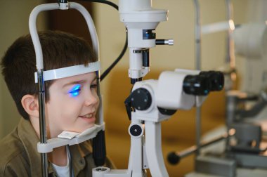 Gülümseyen çocuk, klinikteki modern göz teçhizatından mavi ışıkla görme kontrolünden geçiyor.