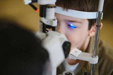 Genç bir çocuk modern bir göz hastalıkları cihazıyla göz muayenesinden geçiyor, tıbbi bir klinikte özel bir vizyon tedavisi görüyor.
