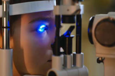 Biçimsiz bir lamba biyomikroskobuyla göz muayenesi geçiren genç bir çocuk modern bir klinikteki bir göz doktorundan özel bir göz bakımı görüyor.