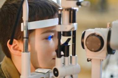 Çocuk modern bir klinikte göz doktoru tarafından kesik lamba biyomikroskobu kullanılarak göz muayenesinden geçiriliyor.