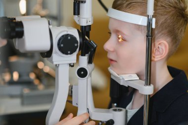 Modern bir klinikte phoropter kullanan bir göz doktoru tarafından görüş kontrolüne tabi tutulan genç bir çocuk.