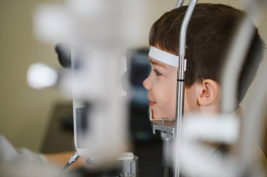 Görme engelli çocuk görme kliniğinde phoropter kullanan bir göz doktoru tarafından kontrol ediliyor.