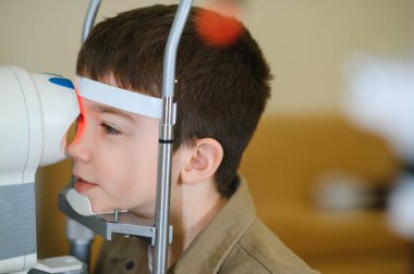 Çocuk hasta vizyonunu bir göz doktoru tarafından kontrol ettiriyor. Görme kliniğinde modern bir tıbbi cihaz kullanıyor.