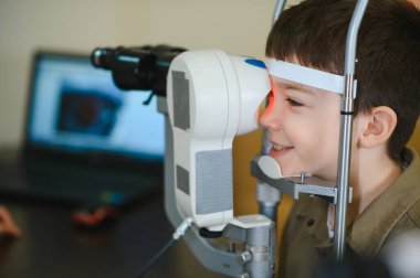 Gülümseyen çocuk, modern bir göz kliniğinde otomatik fraktör kullanan bir göz doktoru tarafından kontrol ediliyor.