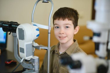 Modern bir klinikte profesyonel oftalmolojik ekipman kullanılarak vizyon teşhisi konan gülümseyen çocuk