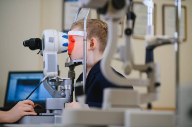 Bir çocuk tıbbi klinikte modern bir tıbbi cihaz kullanarak bir göz doktoru tarafından muayene ediliyor.