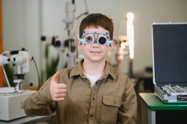 Göz muayenesi sırasında göz farı takan genç bir çocuk göz doktorunun muayenehanesinde olumlu geri bildirim gösteriyor.