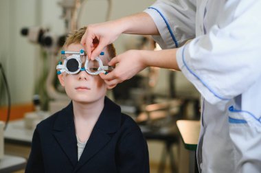 Oftalmolog, göz hekimliği kliniğinde görme testi sırasında genç bir çocuğu dikkatlice test ediyor.