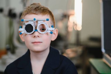 Göz muayenesi sırasında göz çerçevesi takan bir çocuk, bir göz doktorunun ofisinde, özel ekipmanlarla görme ve göz sağlığını değerlendirir.