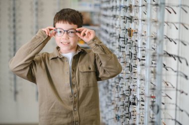 Optik mağazada yeni gözlük deneyen gülümseyen çocuk gelişmiş görüşün tadını çıkarıyor ve seçiminden memnuniyetini dile getiriyor.