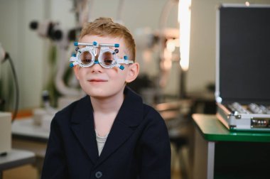 Deneme çerçevesi takan, göz muayenesinden geçen bir çocuk hasta, bir göz doktorunun ofisinde, görme sağlığını değerlendirmeye odaklanmış,