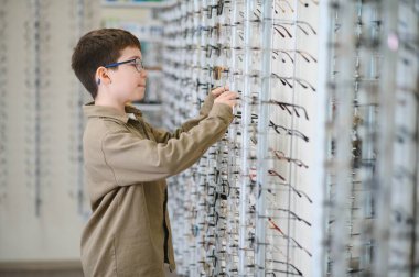 Bir optik mağazasında gözlük takan çocuk, daha net bir görünüm için hazırlanırken çeşitli şık çerçeveleri ve lensleri keşfediyor.