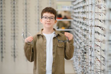 Gözlüklü çocuk optik mağazada, göz doktorunda ve sağlık hizmetleri konseptinde yeni gözlük seçiyor.