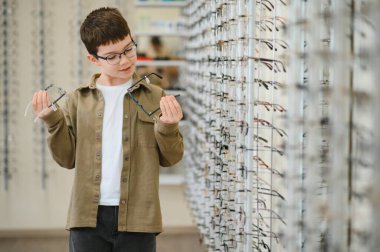 Çocuk bir optik mağazada iki gözlük çerçevesini karşılaştırıyor. Gelişmiş görüş ve tarz için mükemmel bir çift seçiyor.
