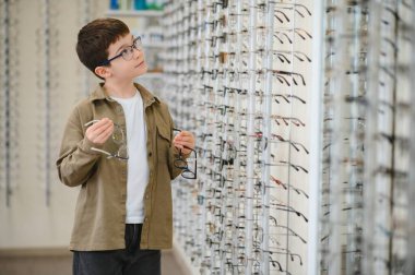 Çocuk bir optik mağazada gözlük karşılaştırma, göz bakımı, göz hekimliği ve göz sağlığı vurguluyor