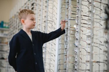 Bir optik mağazada gözlük seçen genç bir çocuk, çocuklar için vizyon bakımının önemini vurguluyor.