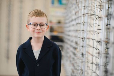 Yeni gözlüğünü takan genç bir çocuk bir optik mağazada gülümsüyor, gözlük, göz doktoru ve sağlık sigortası konseptini seçiyor.