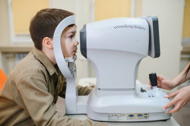 Oftalmolog, modern bir klinikte bir çocuğun görme yetisini otomatik fraktörle inceleyerek, kesin tanı ve göz bakımı sağlar.