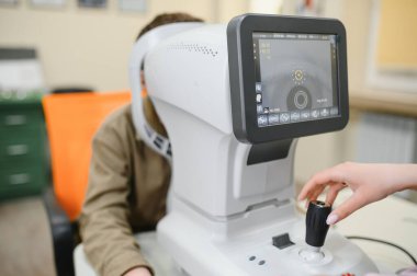 Genç bir çocuğun görme yetisini incelemek için otorfraktometre kullanan doktor, modern göz hastalıkları kliniğinde özel bakım ve tedavi sunuyor.