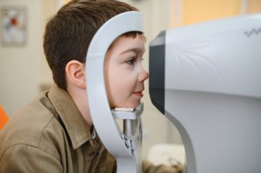 Görme yetisini kontrol ettiren çocuk hasta, göz hekimliği kliniğinde modern bir oto-fraktör kullanarak, doğru teşhis ve tedaviyi sağlama alıyor.